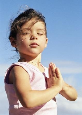 A peaceful child meditating with eyes closed and hands in prayer at heart centre